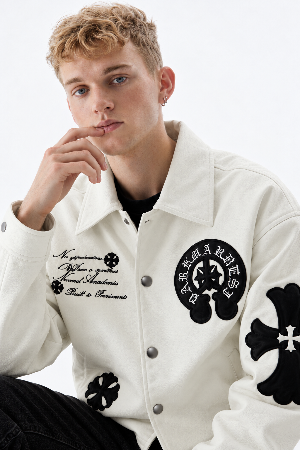Close-up front angle of male model highlighting the silver-tone snap button closures and chest script embroidery on the cream leather jacket