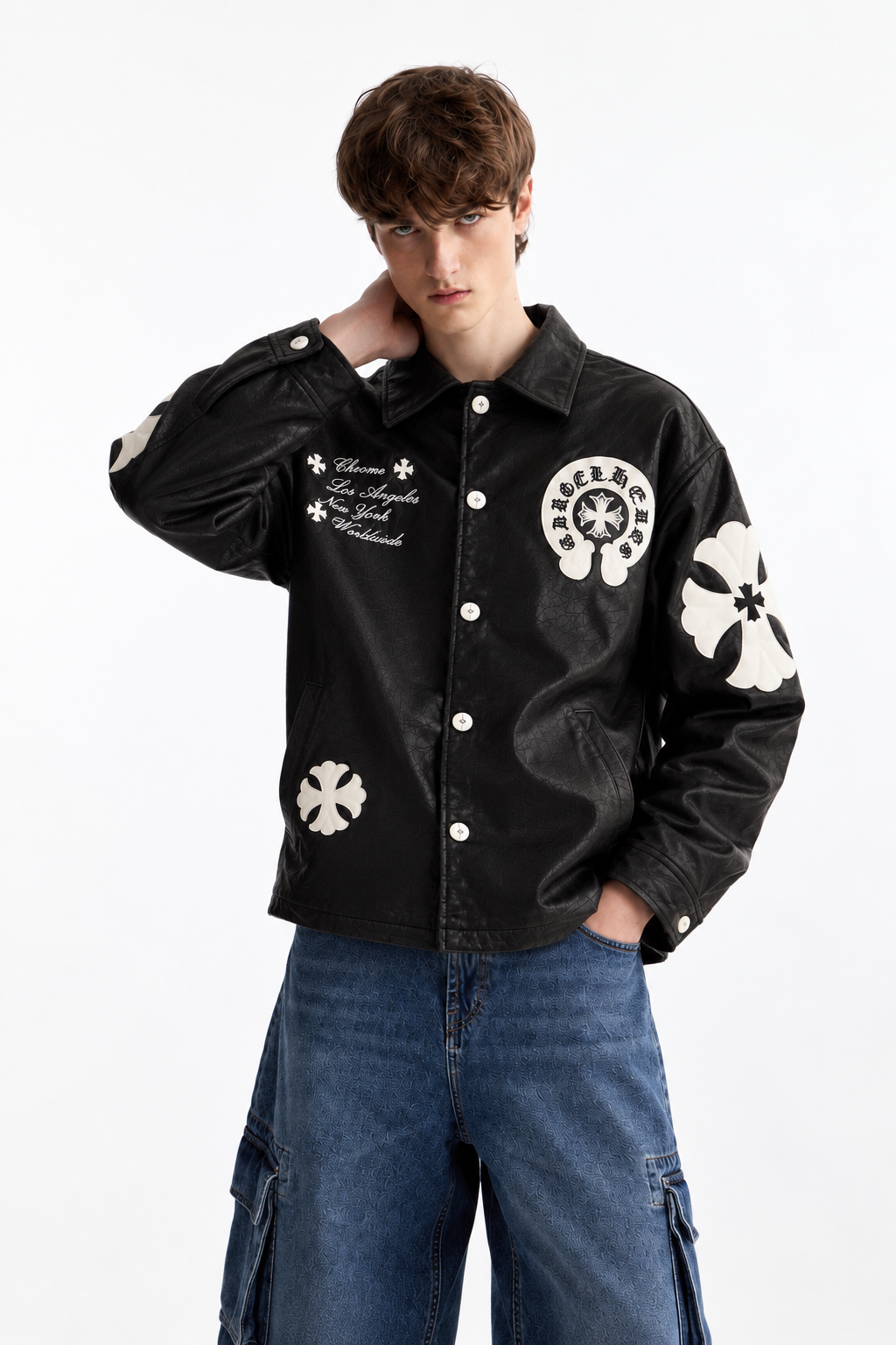 Front view of a boy styling the black cross patch trucker jacket, showing the deep side welt pockets and silver snap fasteners