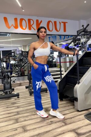 Woman wearing blue Trust Issue Printed Baggy Pants, styled with a white crop top, posing in a gym setting