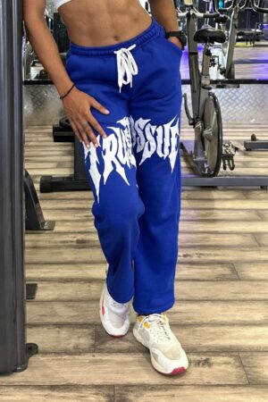 Female model in relaxed-fit Trust Issue Printed Pants, posing casually in a fitness center.