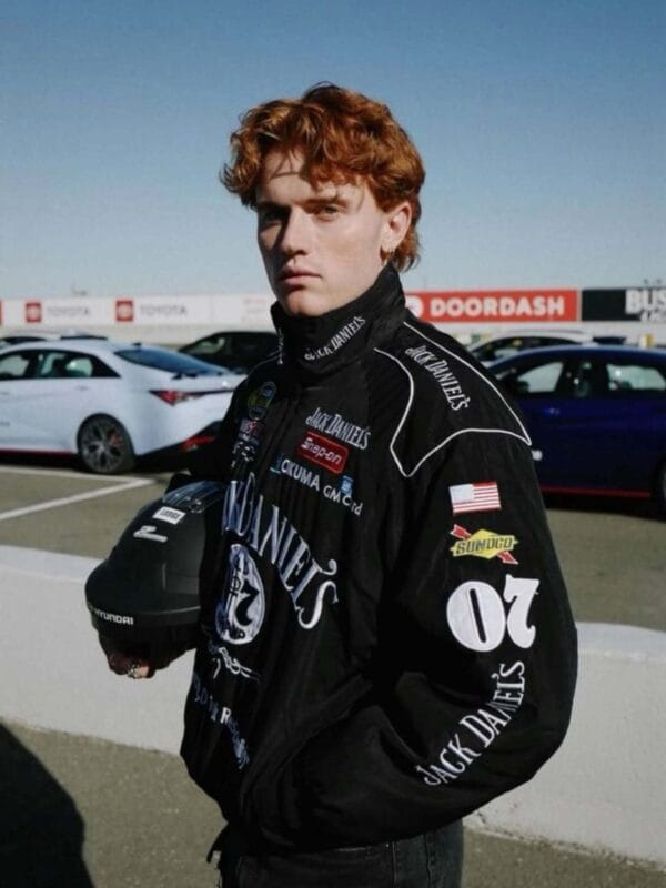 Model wearing a black Jack Daniel's racing jacket with red and black sneakers and a black cap with a red logo. He stands on a street surface looking up at the camera.