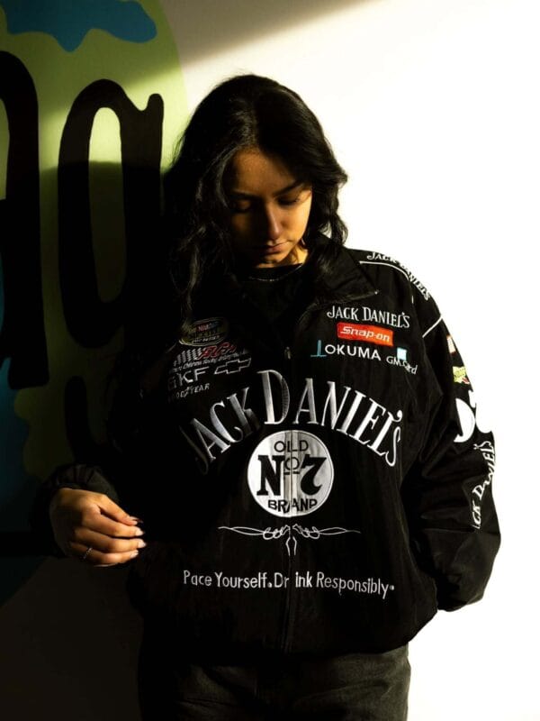 Model wearing a black Jack Daniel's racing jacket over a strappy black top and dress.