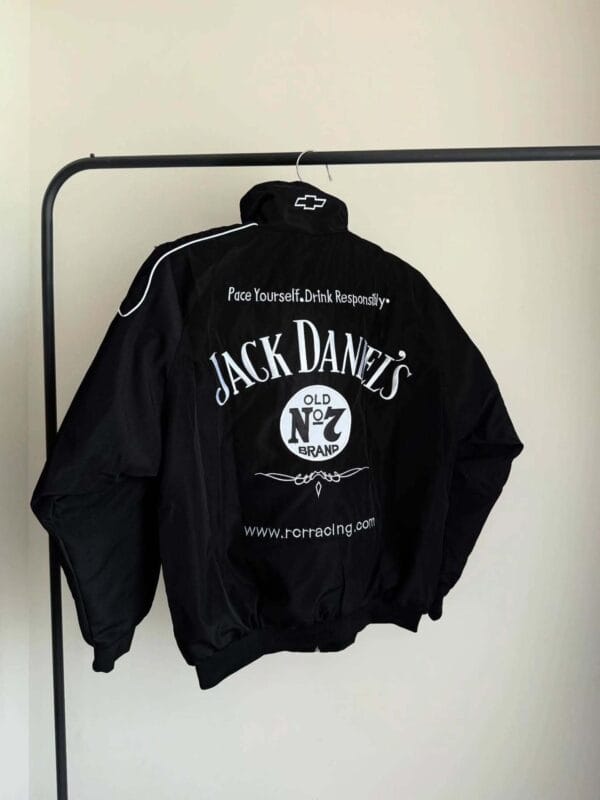 Black Jack Daniel's racing jacket displayed on a clothing rack. The back features bold white "Jack Daniel's Old No. 7 Brand" text, a Chevrolet logo on the collar, and the slogan "Pace Yourself. Drink Responsibly."