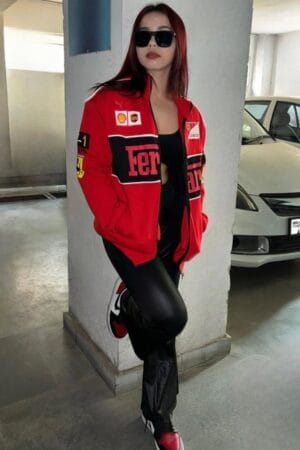 Woman posing in parking area wearing red Ferrari racing jacket, black leather pants, and sneakers, representing premium F1 apparel by Exotix.