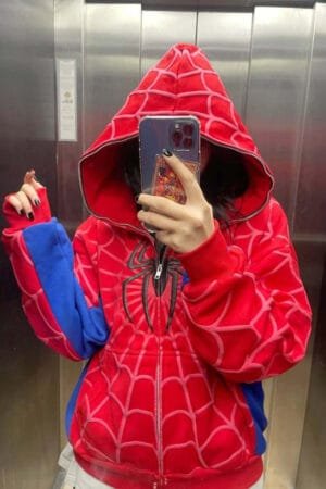 A young woman with long hair takes a mirror selfie while wearing a red and blue Spiderman-patterned hoodie in an elevator.