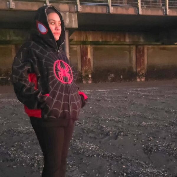 A women poses sideways near a building, highlighting the hoodie’s blue sleeve insert and grey web design on the side panel.