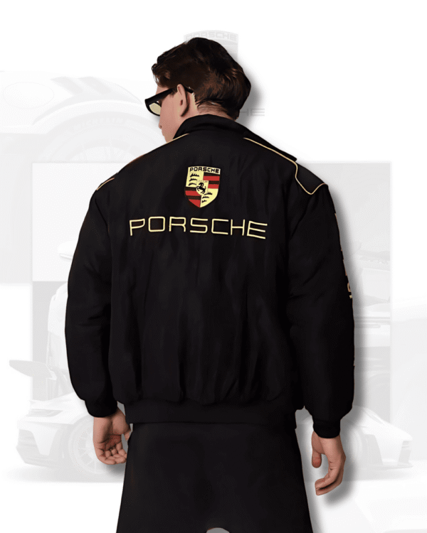 Blonde woman wearing Exotix Porsche bomber jacket with yellow F1 racing embroidery, styled with black top and denim jeans.