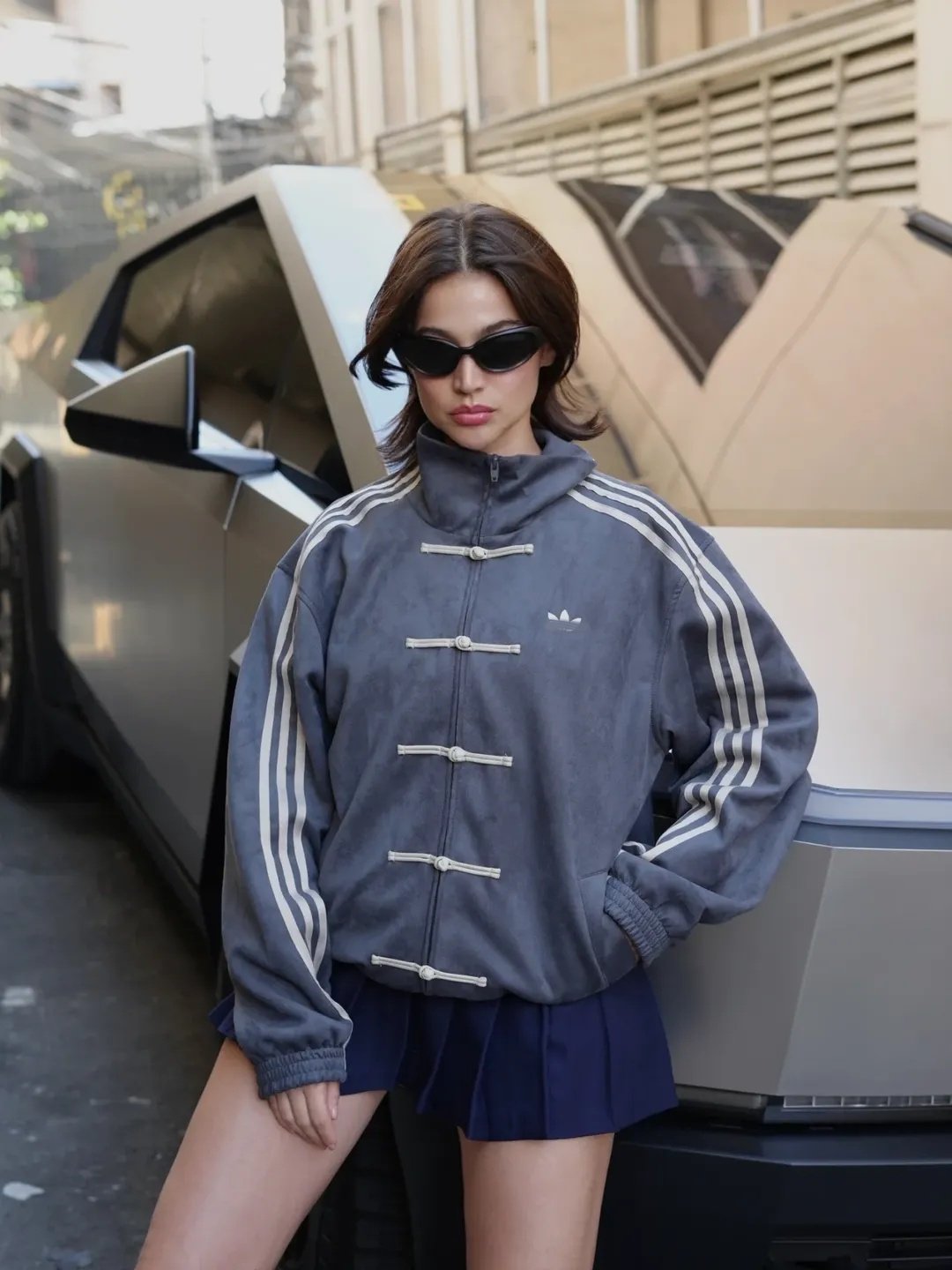 Chinese New Year Jacket – Exotix CNY Edition Fashion model in dark grey Exotix Chinese New Year jacket with classic toggle fastenings and athletic stripe accents, styled with mini skirt and sunglasses in an urban setting.