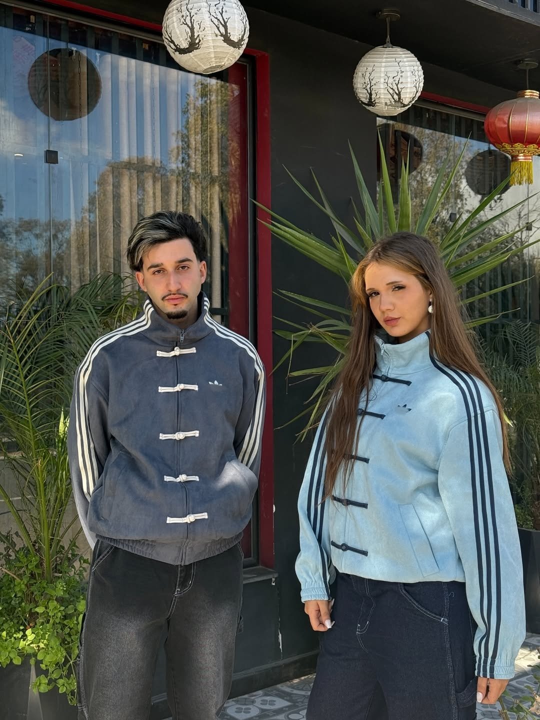 Chinese New Year Jacket – Exotix CNY Edition Male and female models posing outdoors in pastel and grey Chinese New Year Jacket by Exotix, featuring traditional frog button details and sporty side stripes.