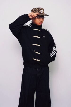 Black CNY jacket front view on male model styled with wide-leg dark denim and leopard print cap — Exotix Tang style oversized jacket India